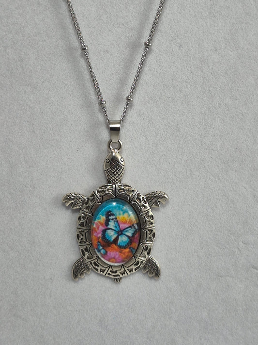 Silver-tone sea turtle pendant with a blue butterfly floral cabochon hanging from a chain.