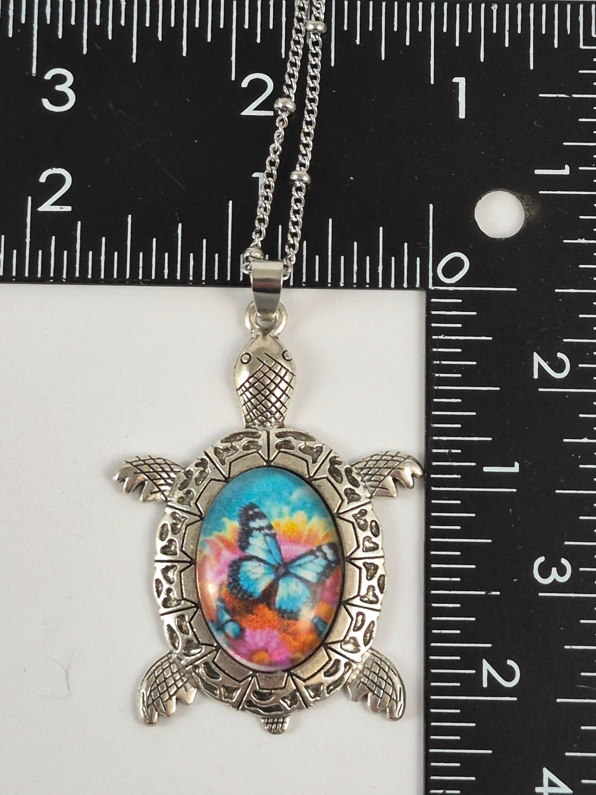 Butterfly floral sea turtle pendant beside a ruler for scale.