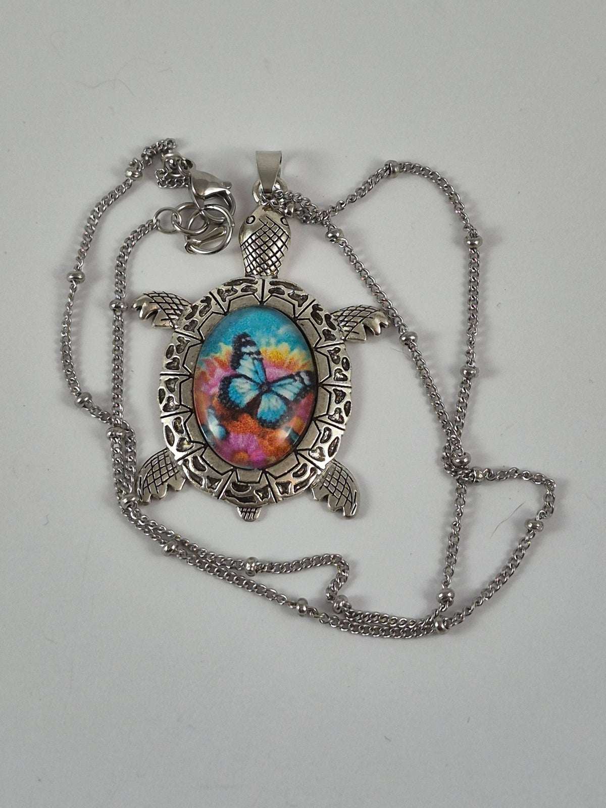 Blue butterfly sea turtle pendant necklace and silver-tone chain laid out on a pale background.