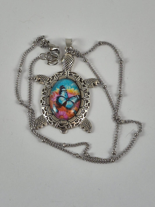 Blue butterfly sea turtle pendant necklace and silver-tone chain laid out on a pale background.