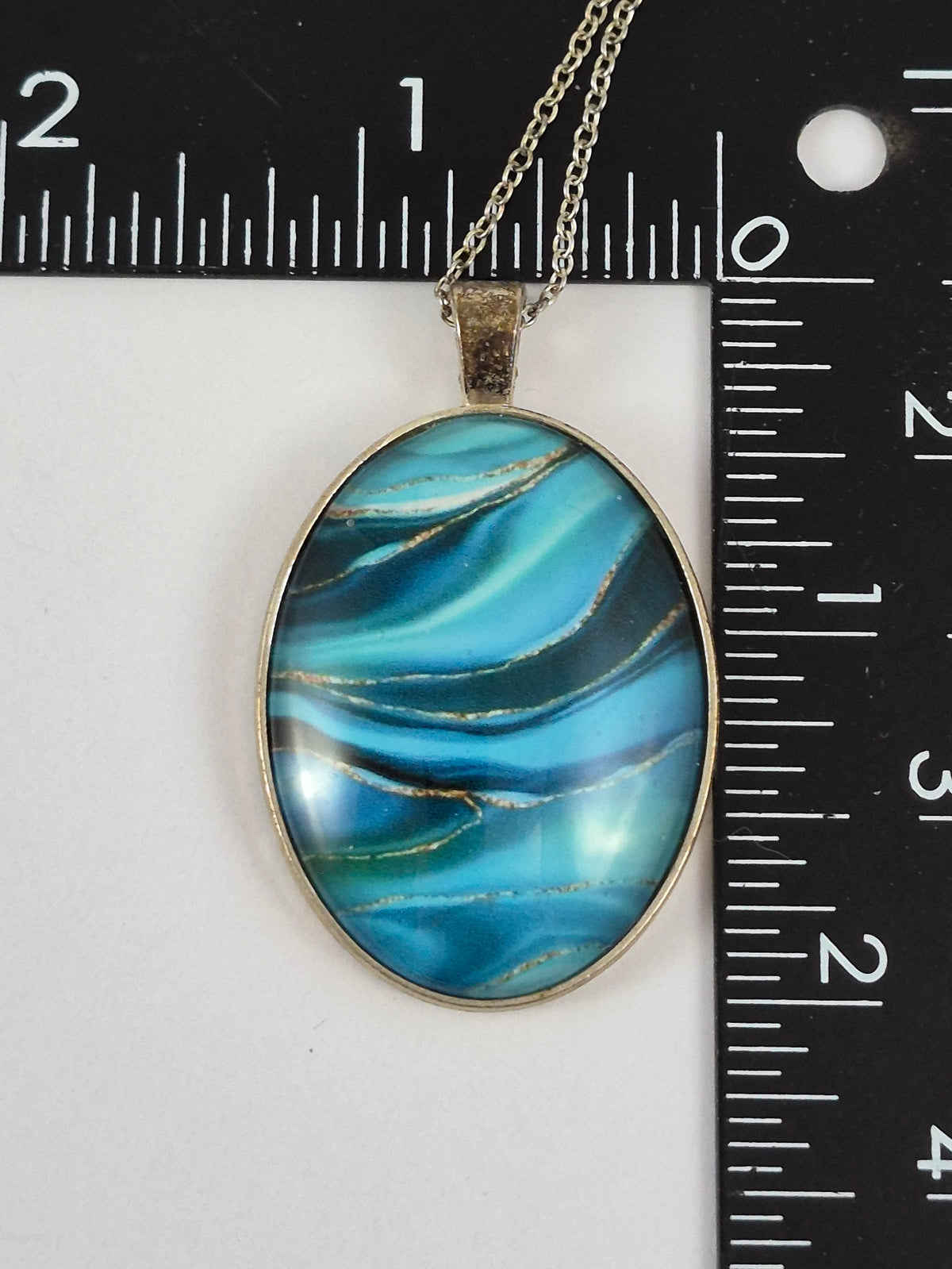 Ocean blue oval cabochon pendant beside a ruler for scale.