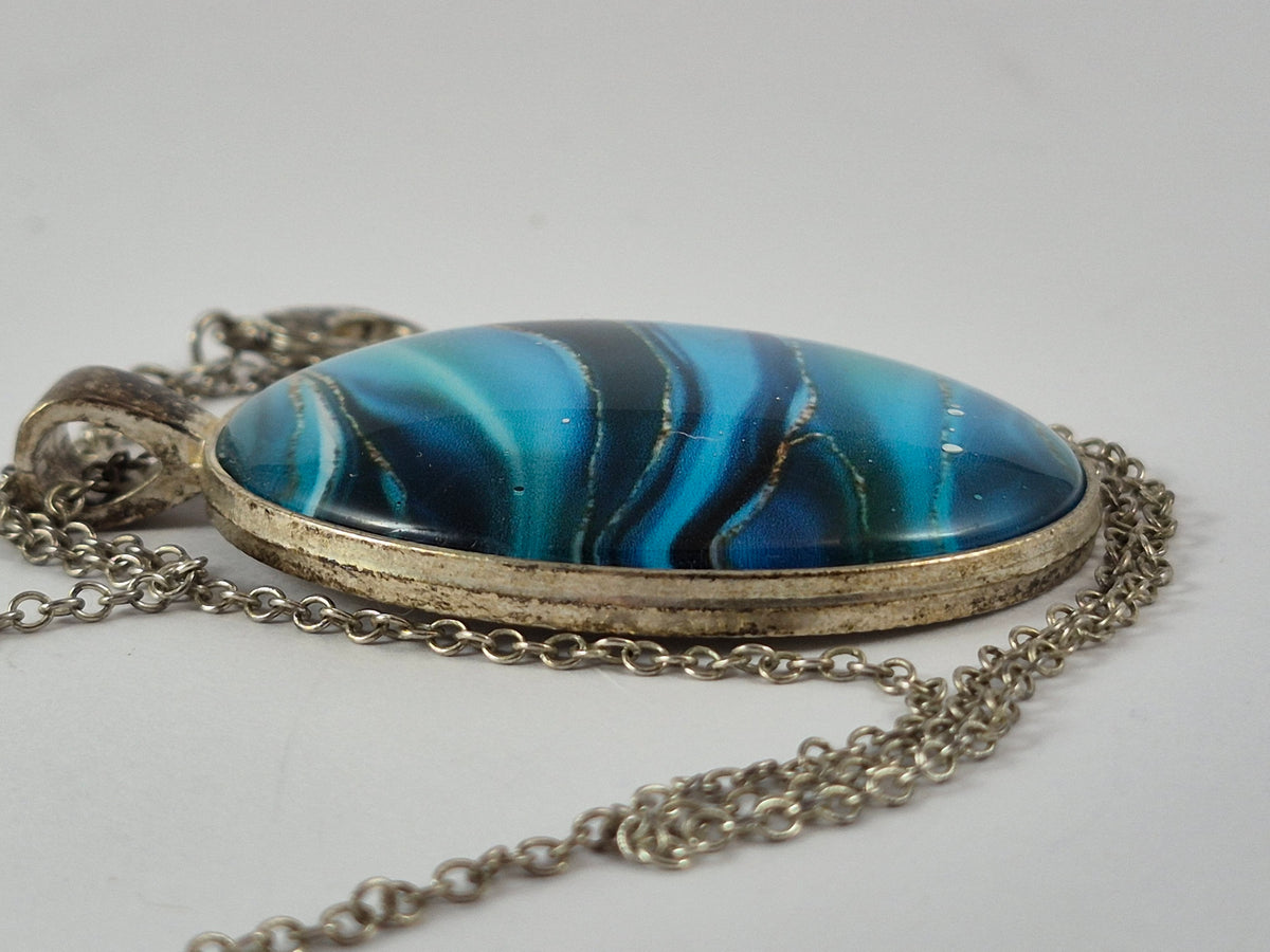 Side view showing the domed blue cabochon and silver-tone pendant frame.