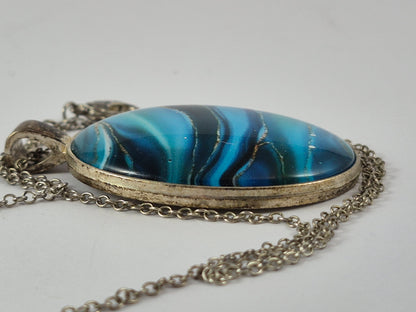 Side view showing the domed blue cabochon and silver-tone pendant frame.