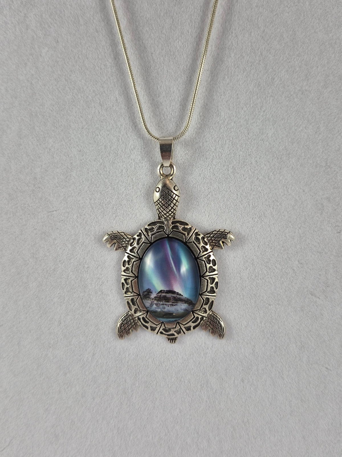 Silver-tone sea turtle pendant with a snowy northern lights scene cabochon hanging on a chain.