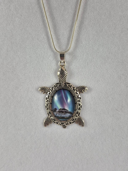 Silver-tone sea turtle pendant with a snowy northern lights scene cabochon hanging on a chain.