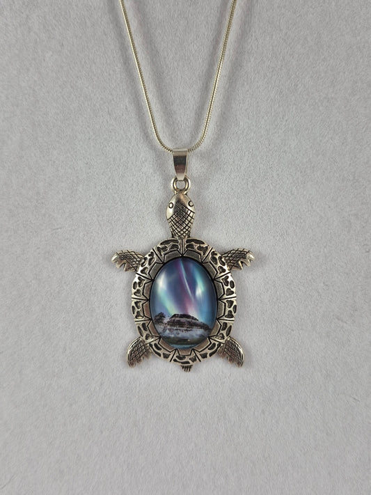 Silver-tone sea turtle pendant with a snowy northern lights scene cabochon hanging on a chain.