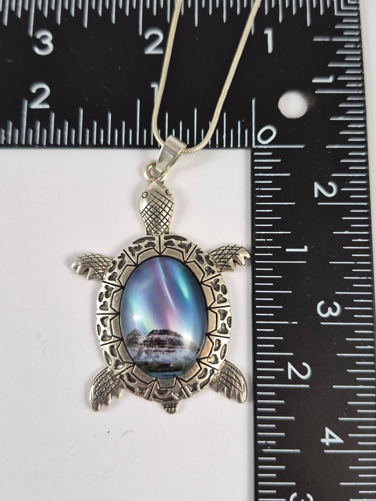 Snowy aurora scene sea turtle pendant beside a ruler for scale.
