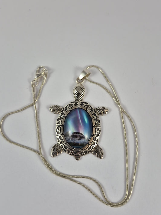 Northern lights sea turtle pendant necklace and silver-tone chain laid out on a pale background.