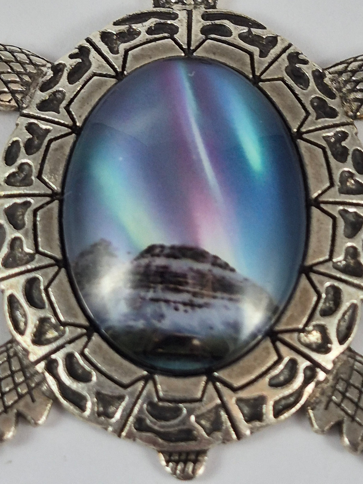 Close-up of northern lights above snow-covered rocks in the oval cabochon of a silver-tone turtle pendant.