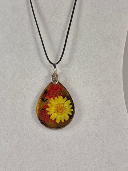 Teardrop resin pendant with a yellow flower and red botanical accents hanging on a black cord.