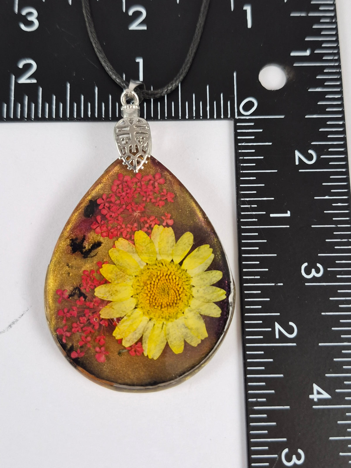 Botanical resin teardrop pendant beside a ruler for scale.