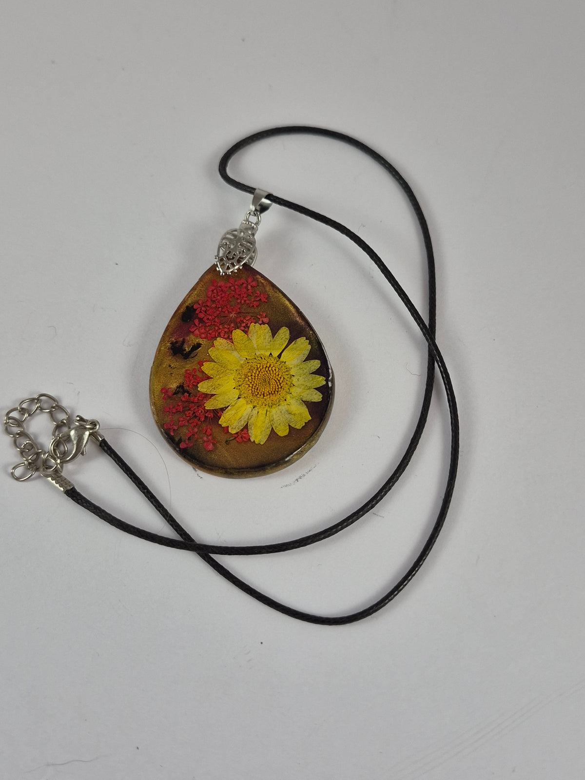 Yellow flower resin pendant with black faux leather cord and extender laid out on white.