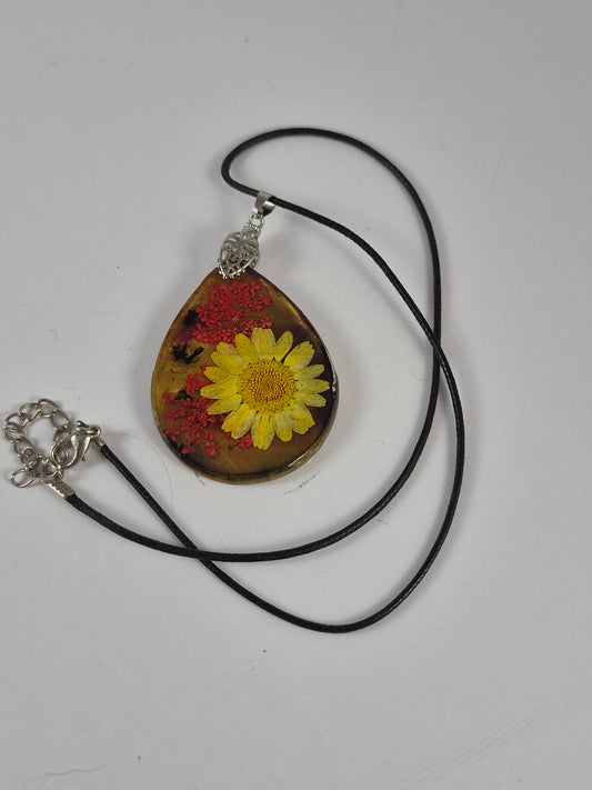 Yellow flower resin pendant with black faux leather cord and extender laid out on white.