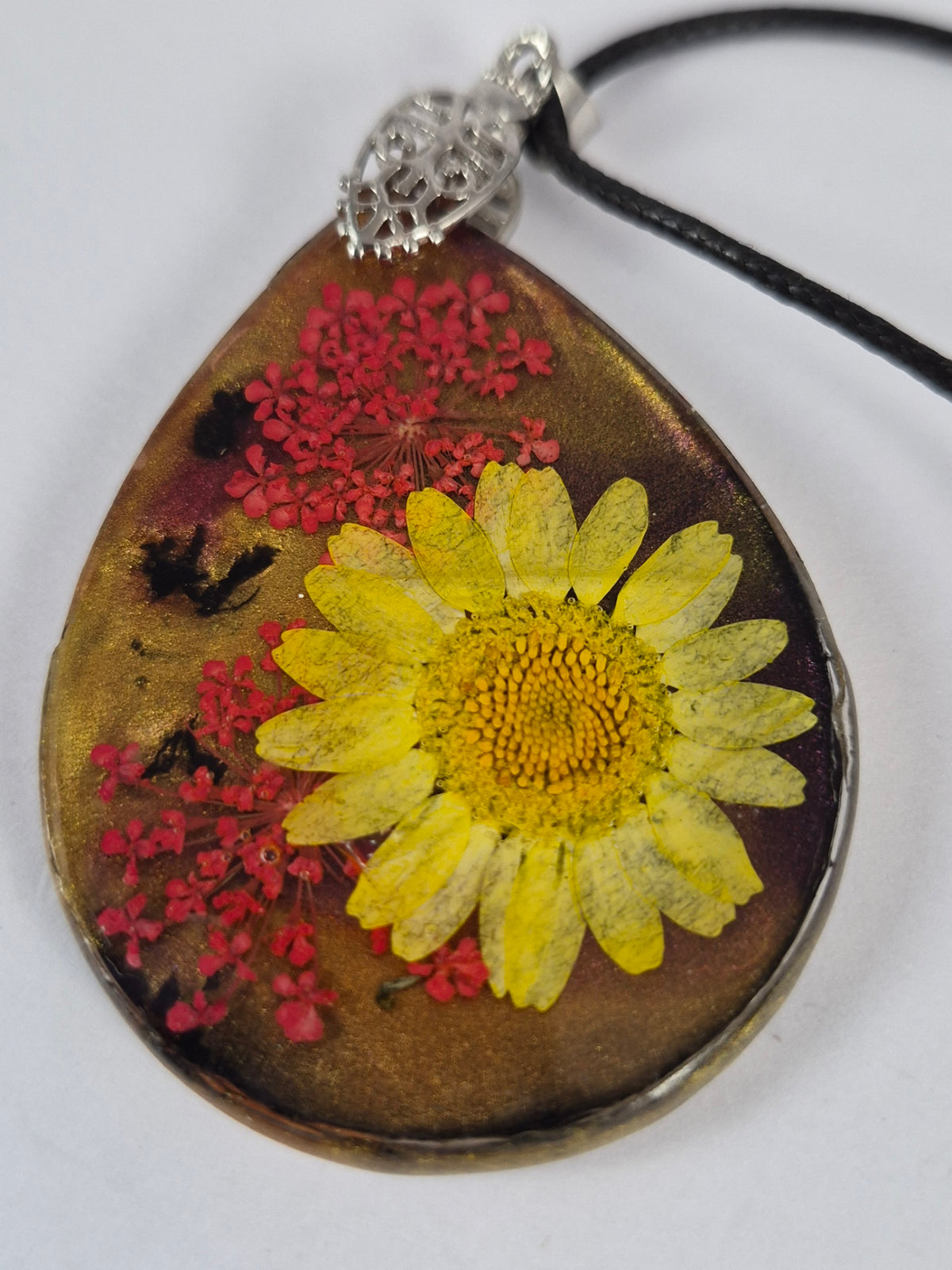 Close-up of the yellow flower and red botanical accents embedded in the resin pendant.