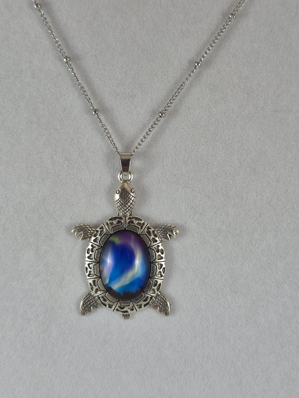 Silver-tone sea turtle pendant with a deep blue northern lights cabochon hanging on a chain.