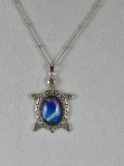 Silver-tone sea turtle pendant with a deep blue northern lights cabochon hanging on a chain.