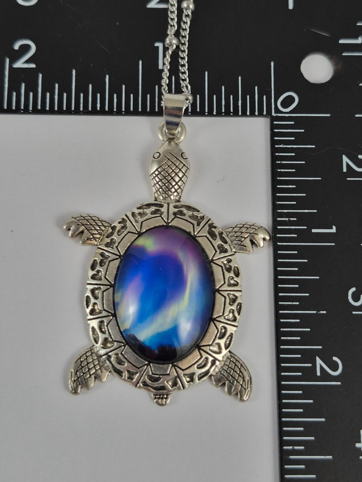 Northern lights cabochon sea turtle pendant beside a ruler for scale.