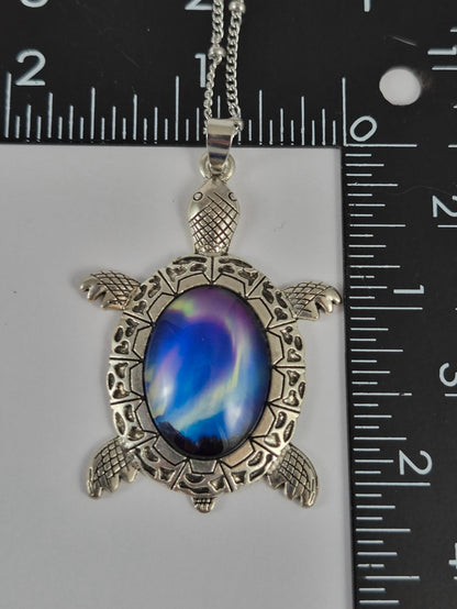 Northern lights cabochon sea turtle pendant beside a ruler for scale.