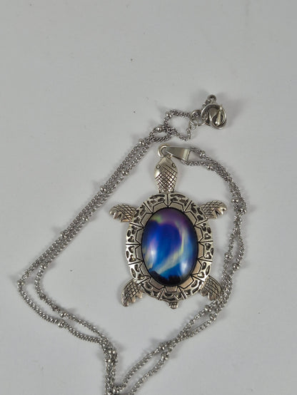 Deep blue aurora sea turtle pendant necklace and chain laid out on a pale background.