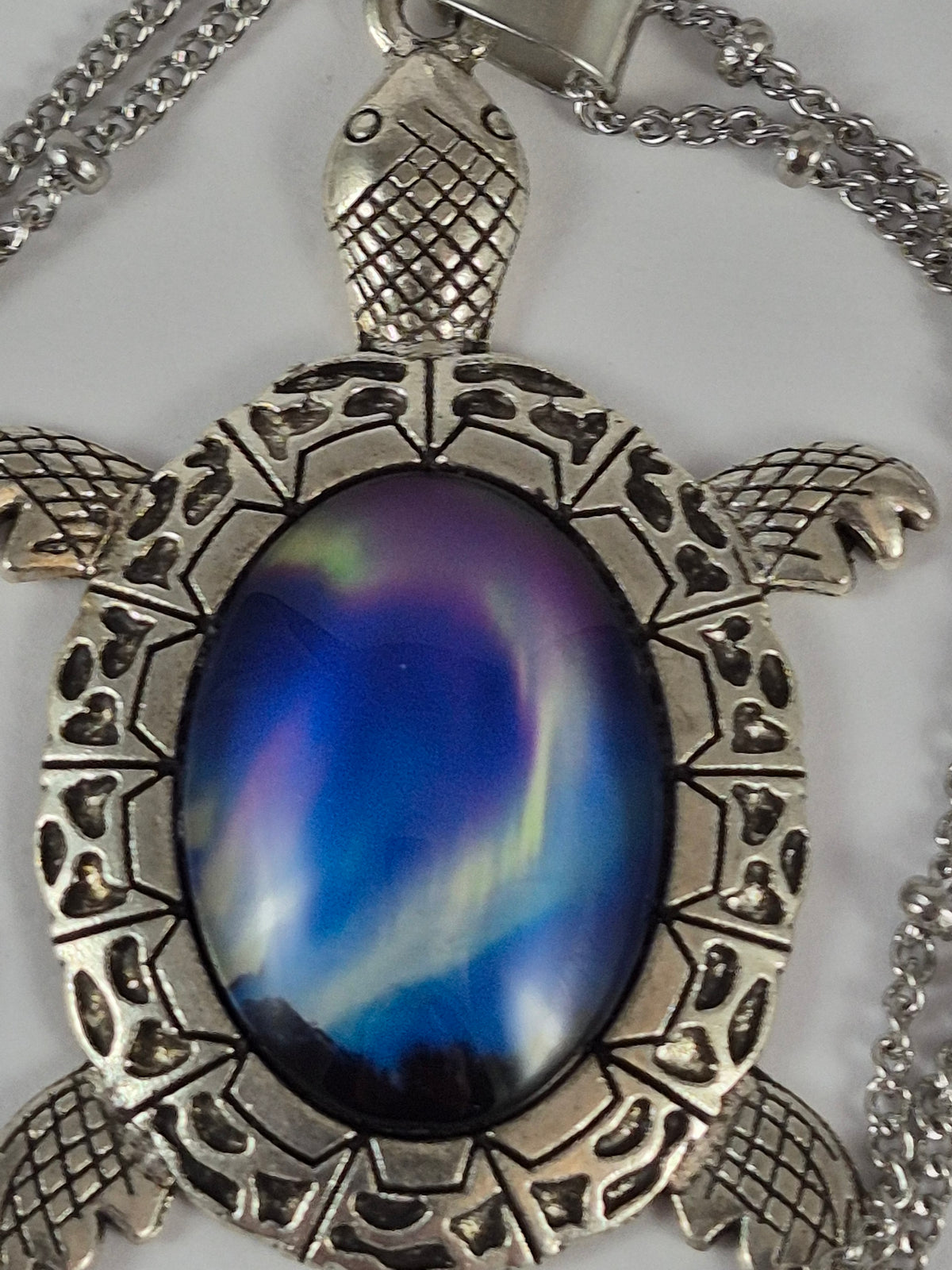 Close-up of blue, green, and purple northern lights in the oval cabochon shell of a silver-tone turtle pendant.