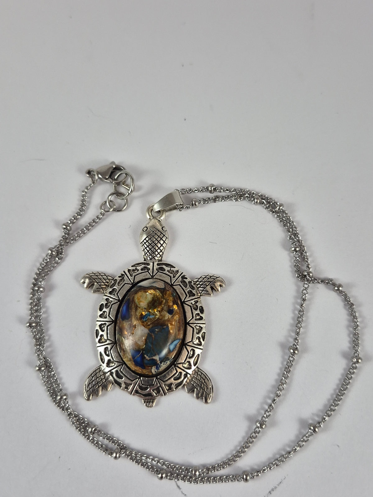 Blue and gold-toned sea turtle pendant necklace and chain laid out on a pale background.
