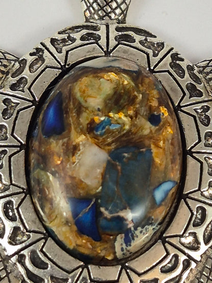 Close-up of blue, cream, and gold-toned details in the oval cabochon shell of a silver-tone turtle pendant.