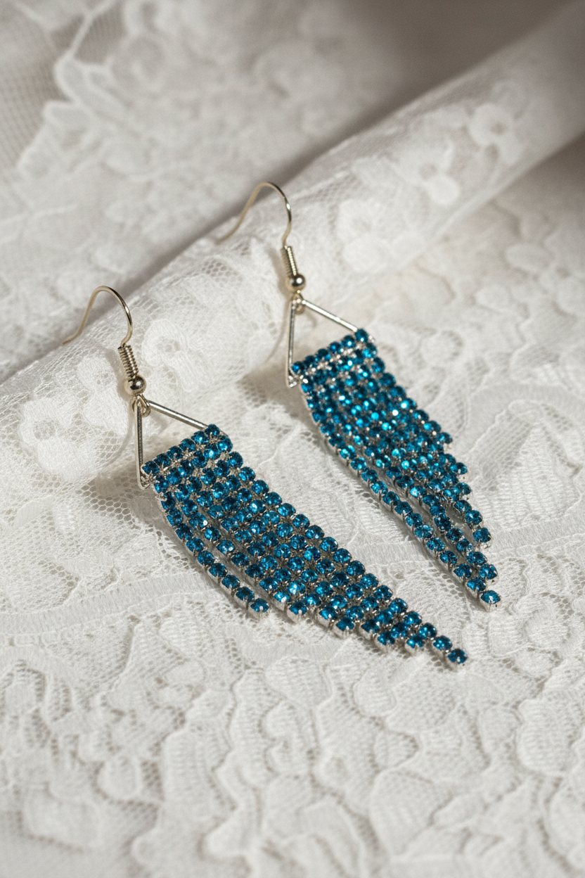 Teal rhinestone fringe earrings on white lace, angled detail view