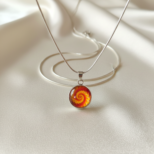 Close-up of glass dome cabochon orange yellow spiral fractal pendant on satin