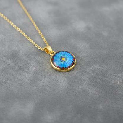 Angled view of petite blue daisy flower pendant on velvet background