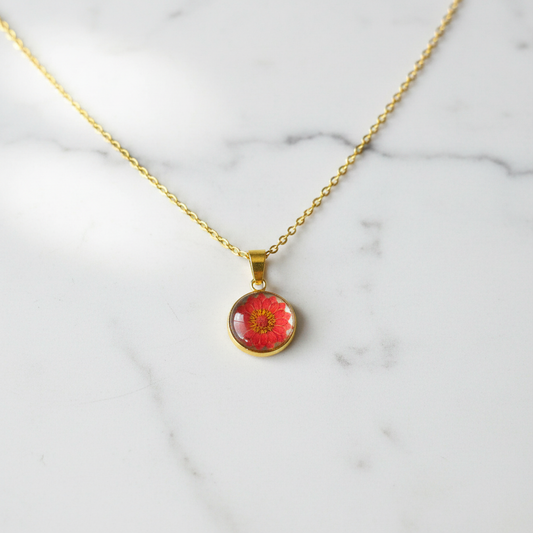 Red zinnia flower petite pendant necklace on white marble surface